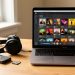 Baladeur MP3 compact posé sur un bureau avec une carte microSD, un casque filaire et un ordinateur portable affichant une bibliothèque musicale visuelle.