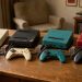 Sélection de consoles de retrogaming, manettes colorées et cartouches de jeux disposées sur un bureau en bois.